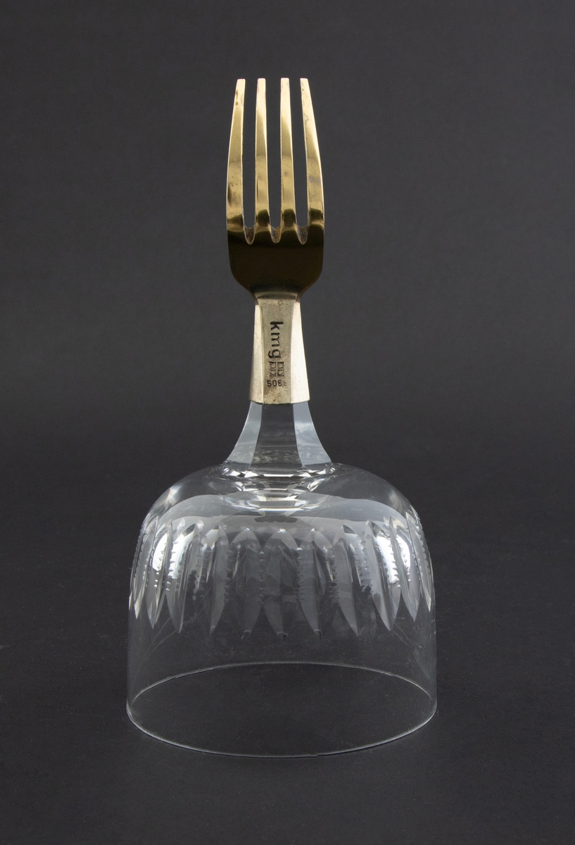 Objektet består av en halv forgylt gaffel som er montert på et vinglass med lansettformede slipninger.