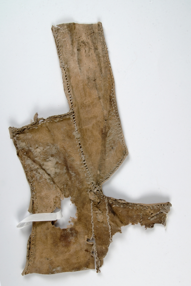 Fragment av pälsplagg, rester av ull på insidan. Sannolikt mansväst med halv ståndkrage och en liten del av framstycket med ärmringing och ett knapphål.