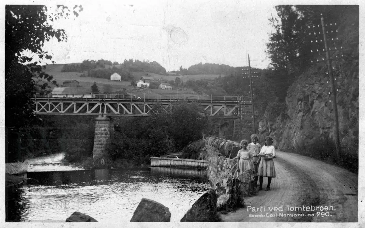 Tomtebroen, en jernbanebro på Røykenvikbanen. Tre jenter står ved en stabbestein ved veien og elva Vigga.Husmannsplasser i Julibakka i bakgrunnen.
