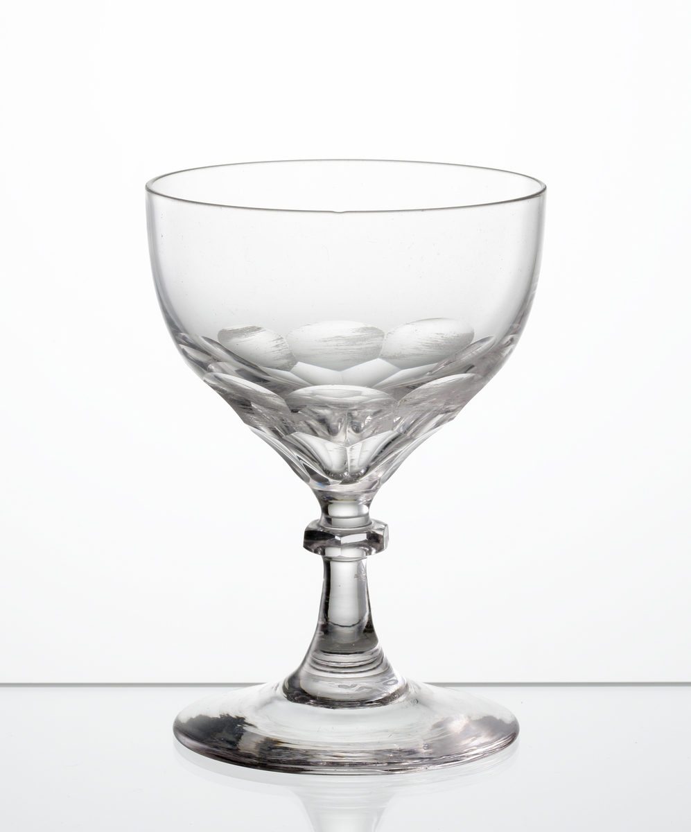 Design: Edward Hald. 
Sherryglas, klotsegmentformad kupa insvängd mot botten. Fasettslipade fjäll på kupans nedre del.
Knappben med slät fot.