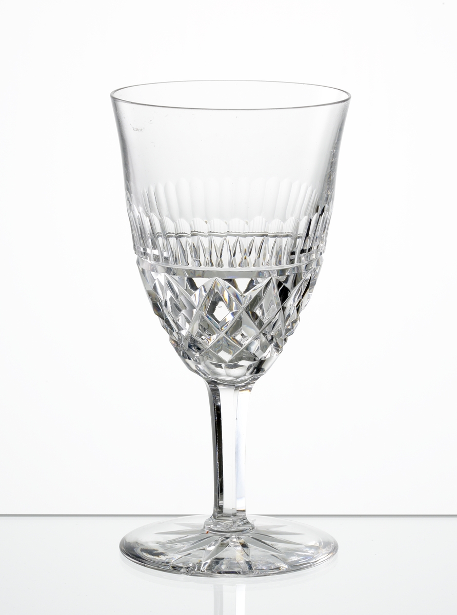 Design: Okänd. 
Vitvinsglas med lätt klockformad kupa, skärslipad nedre del med olivslipad bård. Fasettslipat ben. Fot med skärslipad
stjärna i botten.