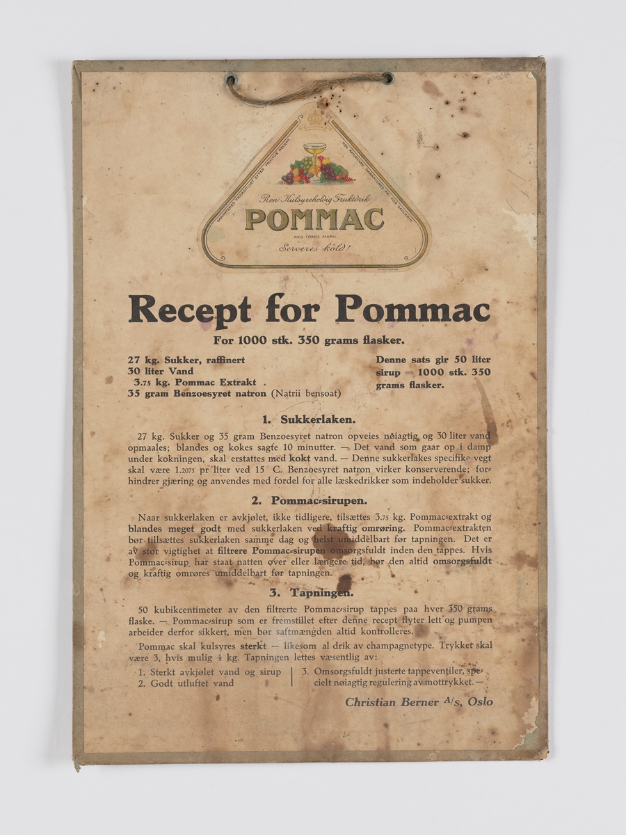 skrift, pålimt etikett til varen "Pommac", med stilleben av frukt og et stettglass