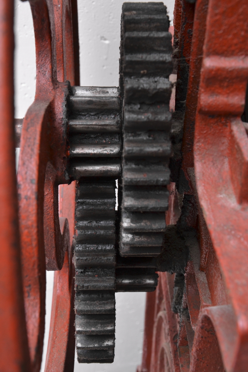 Klesrulle i rødlakkert støpejern på fire hjul. På toppen av klesrullene er det en større justeringsskrue. To større brudd i nedre delen.