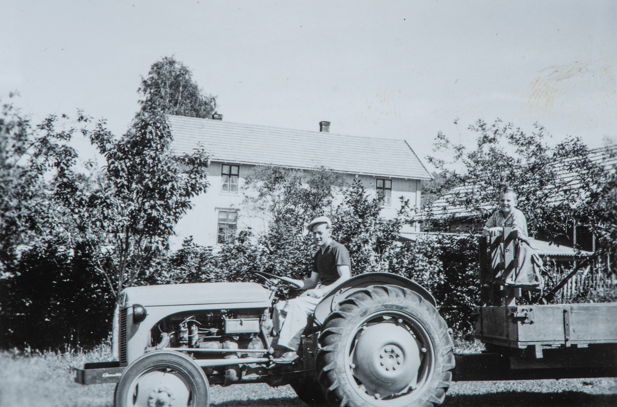 Per Mæhlum med inyinnkjøpt traktor, en Massey Fergusson, gråtass. Sønnen Øystein Mæhlum står bak på tilhengeren. 1959. Huset i bakgrunnen er Bedehuset.