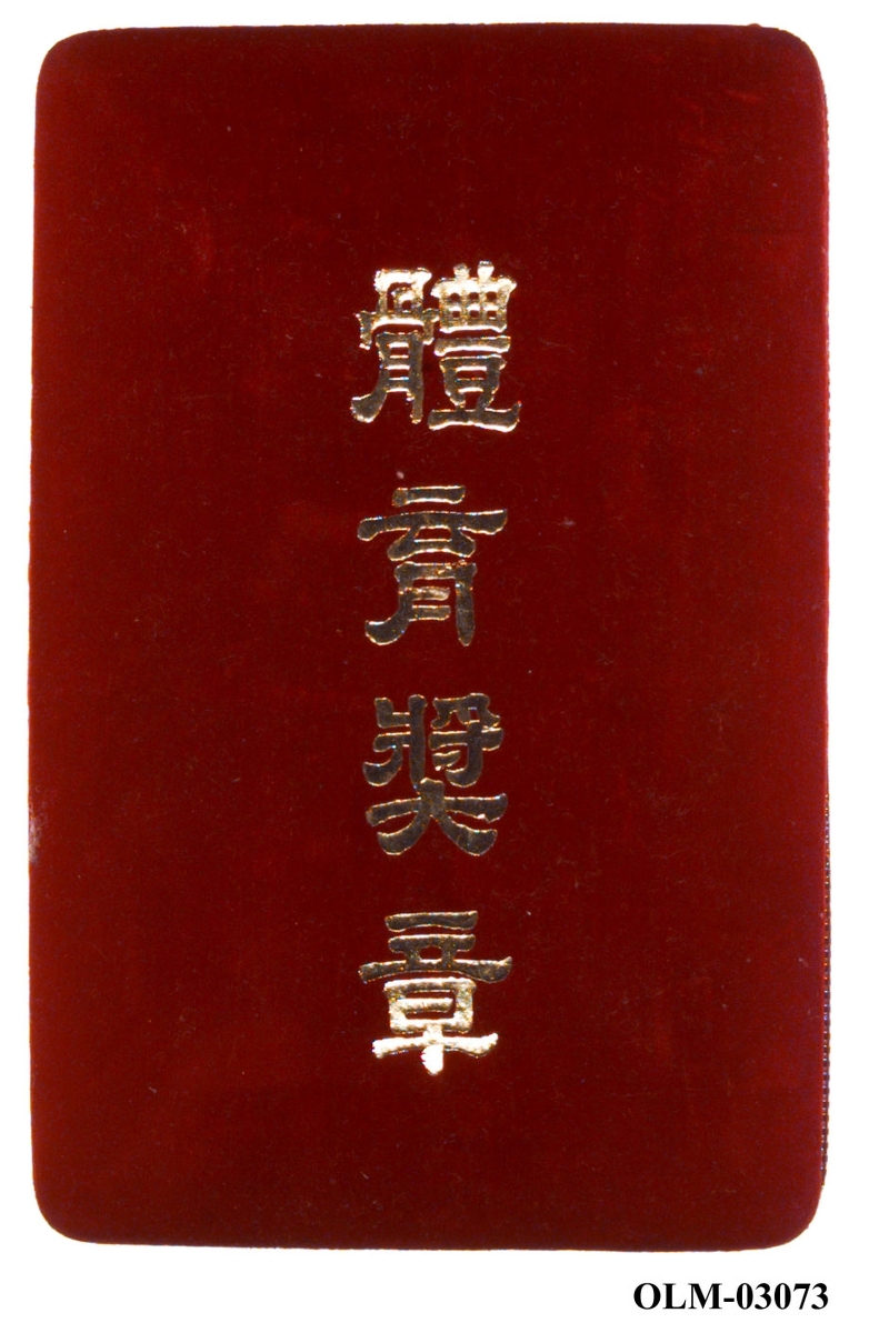 Eske trukket med rød fløyel og med kinesiske tegn på lokket. Esken har hvitt silkefór i lokket og rød fløyelsepute.