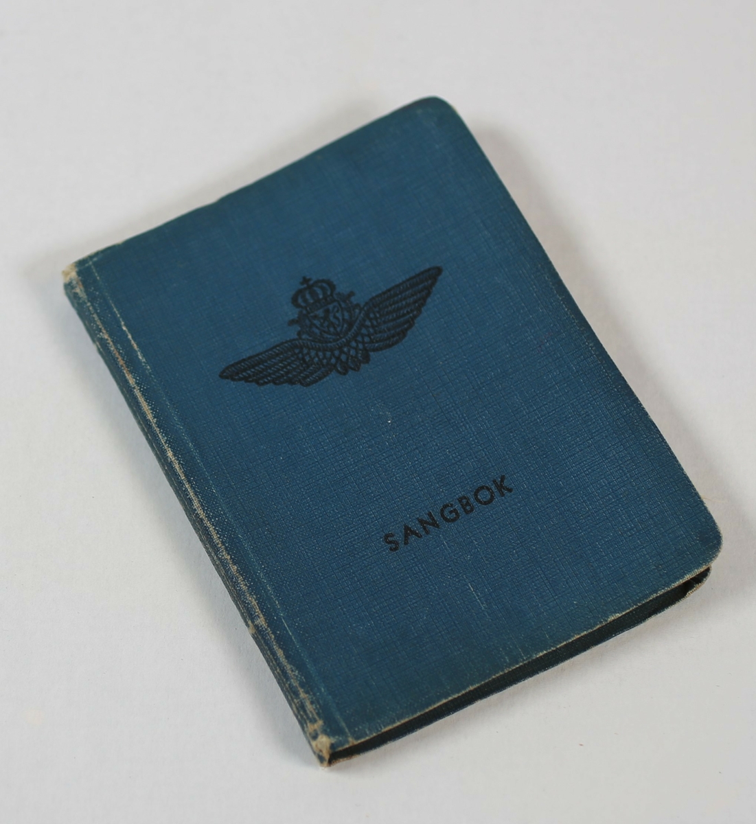 Sangbok fra 2. verdenskrig med vingeemblem og håndskrevet tekst på siste side, skrevet inn med blyant.
