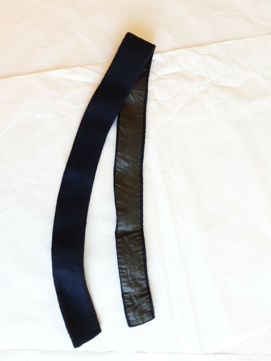 
Belte:l. 95 cm, b. 4, 5 cm. Klede, blått, baksiden foret med grått, glanset lerretsstoff. 2 metallhekter, 2 stoffhemper til lukking. Fasongsydd for hånd
