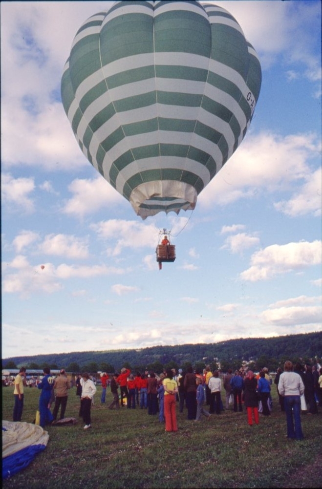 En grönvit-randig luftballong i luften. En folksamling på marken nedanför.