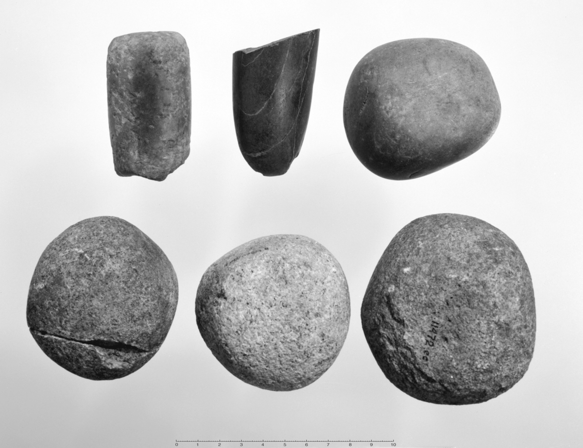 Knusestein av kornet bergart, nærmest kuleformet med kvelvde fasetter, en side viser litt uslitt opprinnelig rullesteinsoverflate. 7,6 til 8,9 cm i tverrmål