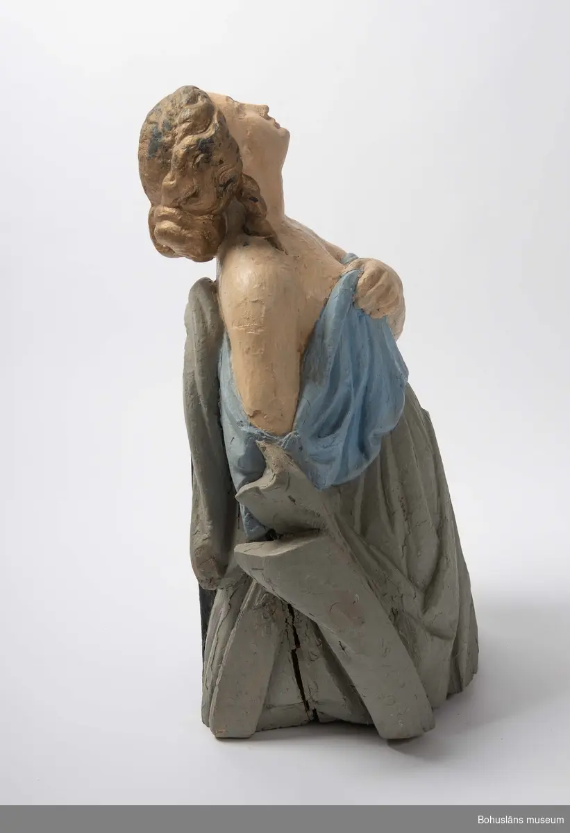 Föremålet visas i basutställningen Kustland,  Bohusläns museum, Uddevalla.

Galjonsfigur från mitten av 1800-talet föreställande kvinnofigur iförd en löst draperad klädnad som bildar böljande veck.  Kvinnan blickar mot skyn, har en uppsatt frisyr med stor knut i nacken och nedfallande lockar vid öronen, nakna axlar och hon håller klänningens överdel med vänster hand över bröstet. Baksidan är  delvis obearbetad.
Figuren är skuren ur ett stycke trä, krederad och bemålad. 
Nuvarande bemålning är med största sannolikhet utförd av C G Bernhardson med håret i guld, klänningens överdel ljusblått, nederdelen grå, baksidan och en del av framsidans nederdel svart.
Nertill på galjonsbildens framsida har Bernhardson skrivit med röda bokstäver: 
"Flamingo Great Britain", troligen namnet på ett fartyg, kanske det som galjonsbilden en gång hört till. Uppgifter saknas om fyndomständigheter.
Upphängningsögla på baksidan med nylonsnöre.
Torrsprickor, färgbortfall som målats över.