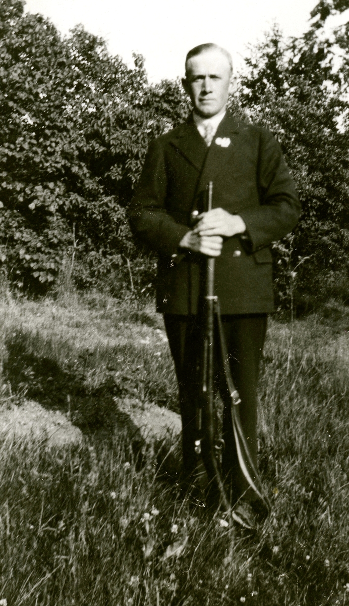 John Johansson (född Backen "Smen" 1898, död 1966 Nygård) poserar på tomten med ett gevär framför sig, Kållered Stom "Nygård" okänt årtal.