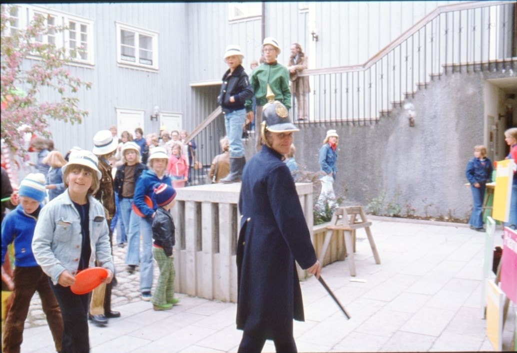Barn på innergården till kv Hjorten söder om Gränna torg. En person går runt i gammaldags polisuniform. Troligen i samband med arrangemanget "Barnens stad".