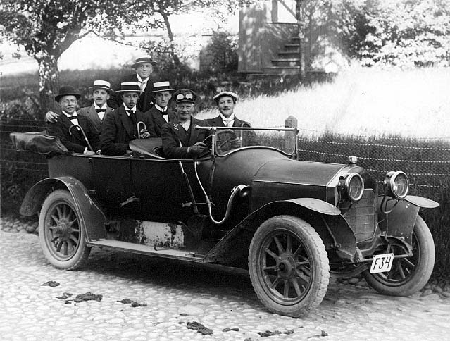 En bil (cabriolet) med registreringsskylt "F34" står på den kullerstensbelagda Brahegatan i Gränna. I bilen sitter det sex män och en sjunde står möjligen på fotsteget på andra sidan av bilen. De är glada. Någon av männen är troligen Emil Nilsson från Huskvarna.