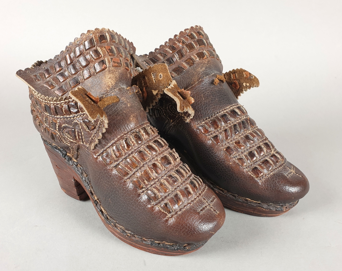 Kopi av sko fra 1700-tallet. Høy hæl og såle av tre. Flettet lær som dekorasjon på over vristen, på tungen og på hælkappen. Randsøm.