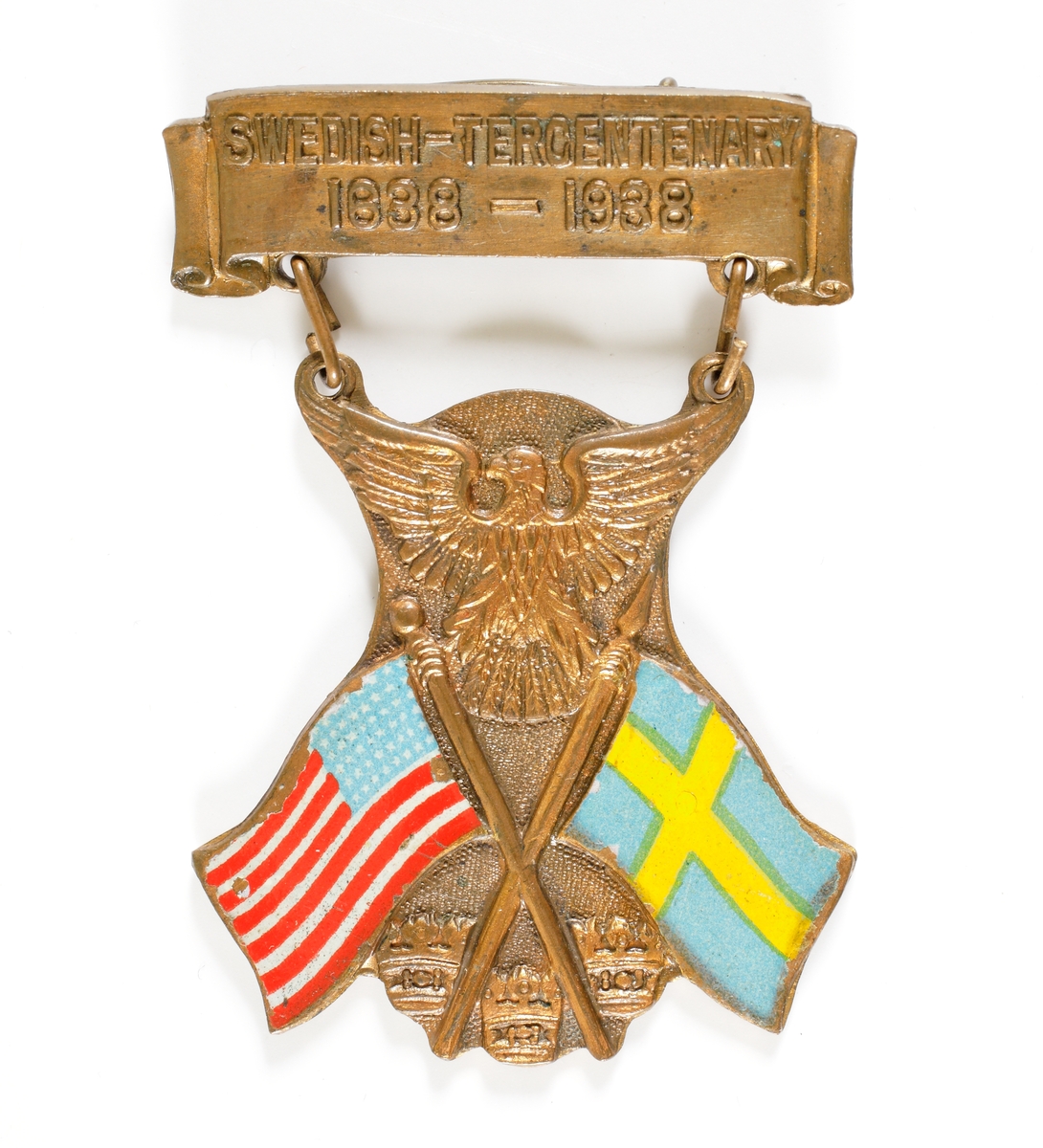 Nålmärke bestående av en överdel försedd med texten "SWEDISH-TERCENTENARY 1638-1938", samt en underdel som är sammanlänkad med två öglor. Den undre delen består av två korslagda fanor, den amerikanska och den svenska, samt upptill den amerikanska nationalörnen och nedtill de tre svenska kronorna.