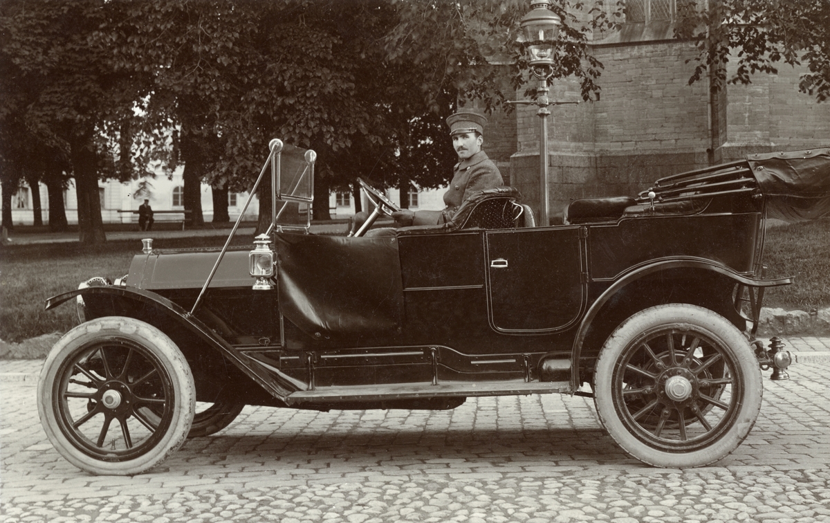 Chauffören Henrik Alm sitter stolt i en Cadillac modell 30 från 1911. Bilen tillhör manufakturhandeln Axel Karlsson & Co där Alm varit anställd sedan omkring 1915. Vid fototillfället har bilen parkerats på Apotekaregatan intill Domkyrkoparken.