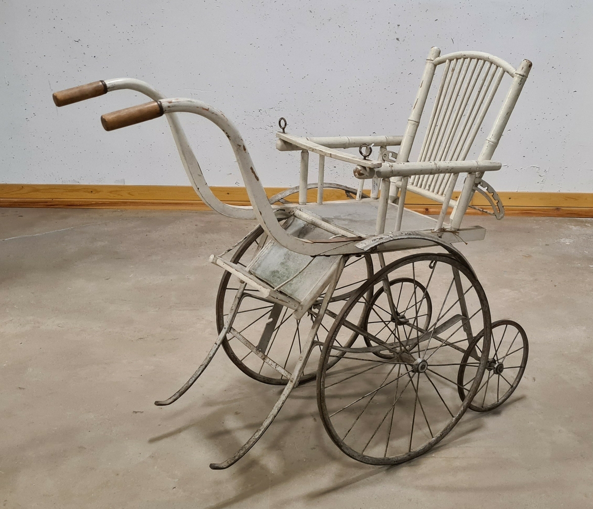 Barnvagn, sittvagn, sittkärra i trä. Kärran har två handtag. Större hjul fram och mindre hjul baktill. Ryggen är reglerbar.