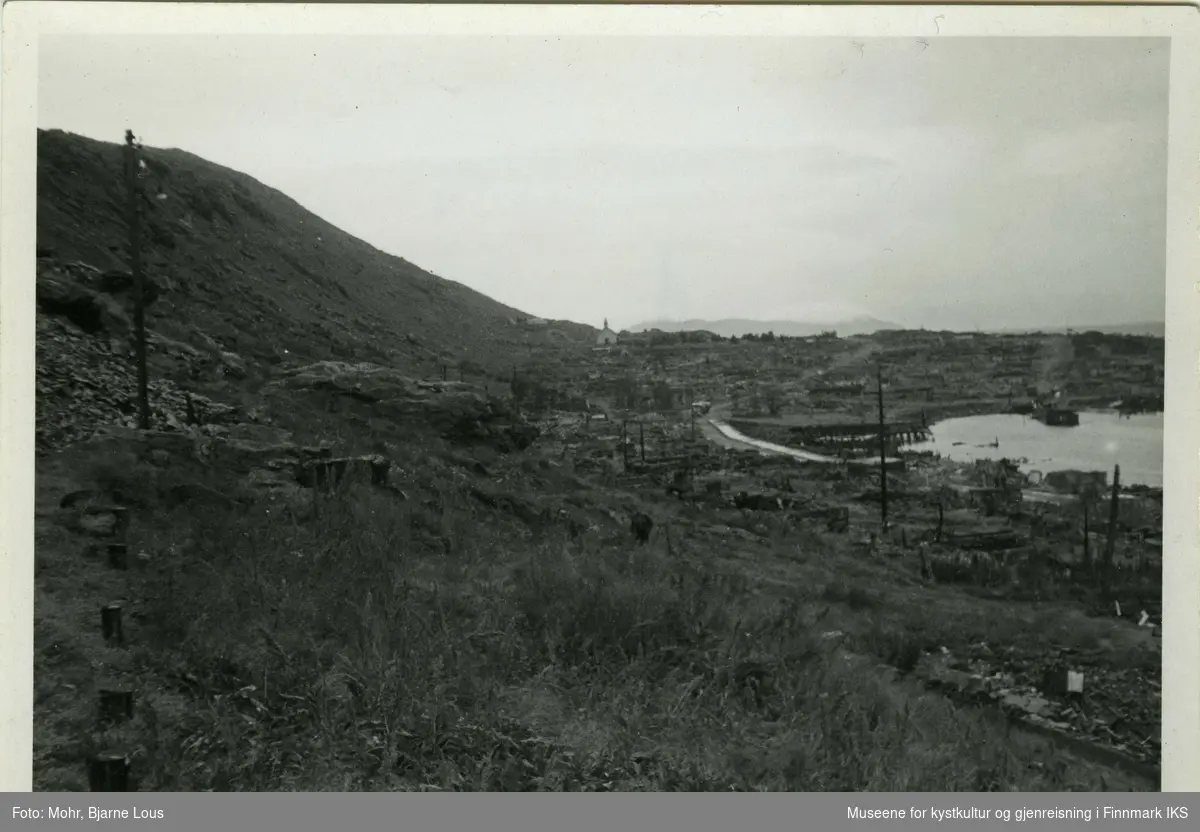 Ødelagt bebyggelse i Hammerfest sentrum og Hauen etter andre verdenskrig. Til venstre i bilde ligger Salenfjellet og man ser en strømstolpe. Helt bak i midten ser man den uskadede kirkegårdskapellen omringet av ruiner. Til høyre ligger rester av ødelagte hus, veier, og kaianlegg i havna.