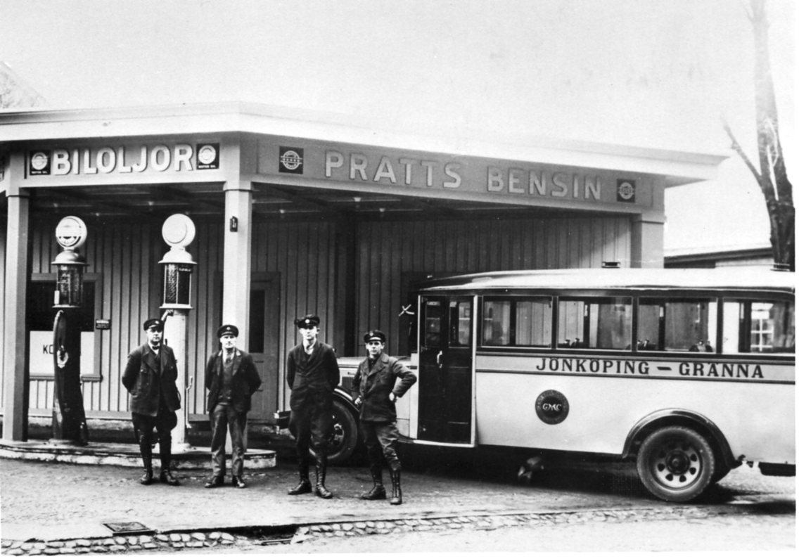 En buss av märket GMC står parkerad vid en Pratts bensinsstation. Bussen är märkt "Jönköping-Gränna" på långsidan. Fyra män i uniformer står vid bussen.
