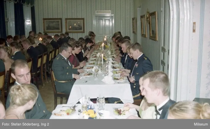 Middagsgäster sittande runt middagsbord. Kapten Lars Persson till vänster om andra bordet.