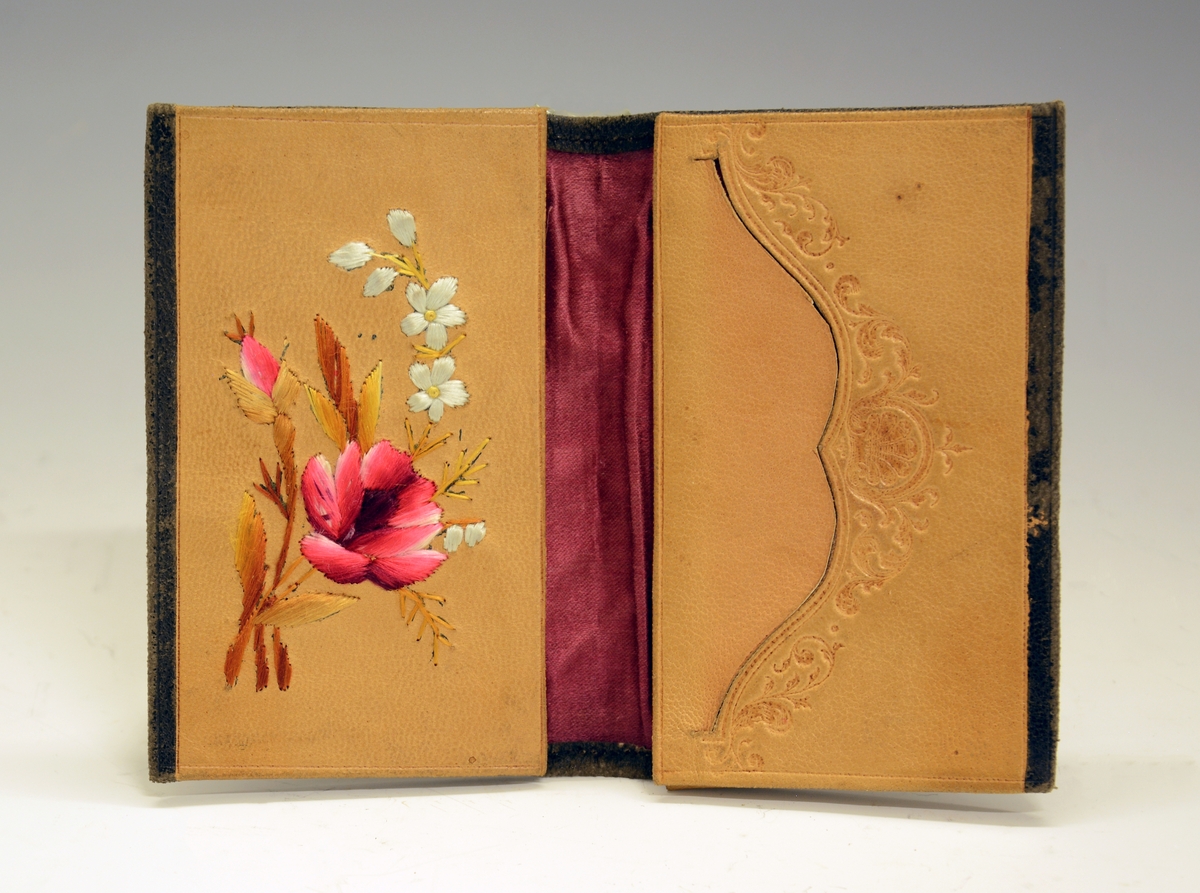 Lommebok. Fra protokollen: Liten lommebok. På utsiden sort, på innsiden lys brunt skinn. På venstre oppslag brodert en blomsterbukett med bl.a. rose. På høyre side en bueformet åpning kantet av et innpresset ornament. Foret med rødt stoff.