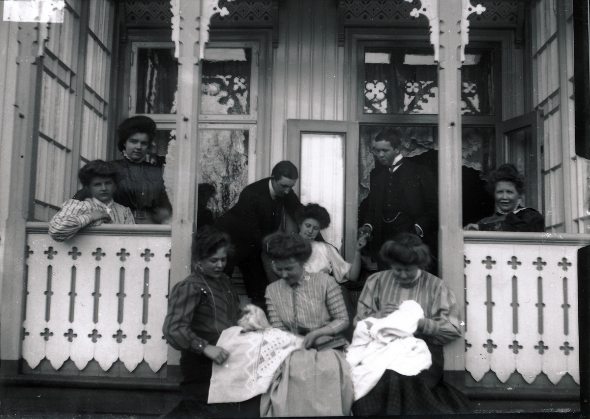 Syv unge kvinner og to unge menn på verandaen ved bestyrerboligen på Kistefos. Tre av kvinnene syr. Mannen til høyre er Harald Rydgren.