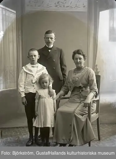 Ateljébild. Familjebild, föräldrar med en liten flicka och en pojke i helfigur där modern sitter. Beställare: Stationsskrivare Helmer.