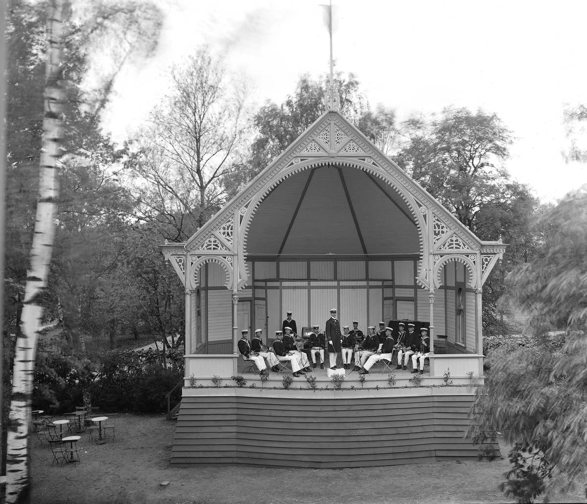 Scenen vid Trädgårdsföreningen i Linköping. Orkester spelar på scenen. 

...

Park. Musikunderhållning. Musik. Paviljong.