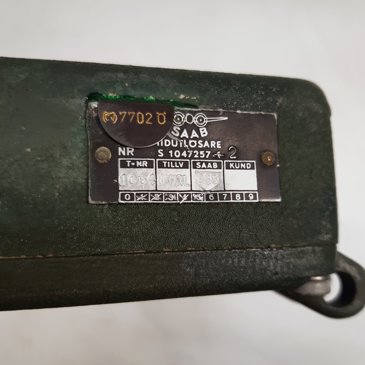 Tidutlösare, Nr S 1047257, i grönlackerad metall och med en inre fjäder-mekanism.