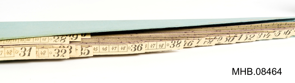 Svart eske med rekangulært snitt, todelt, og hvor den ene delen inneholder papirremser (skjema) med tall med kolonner.