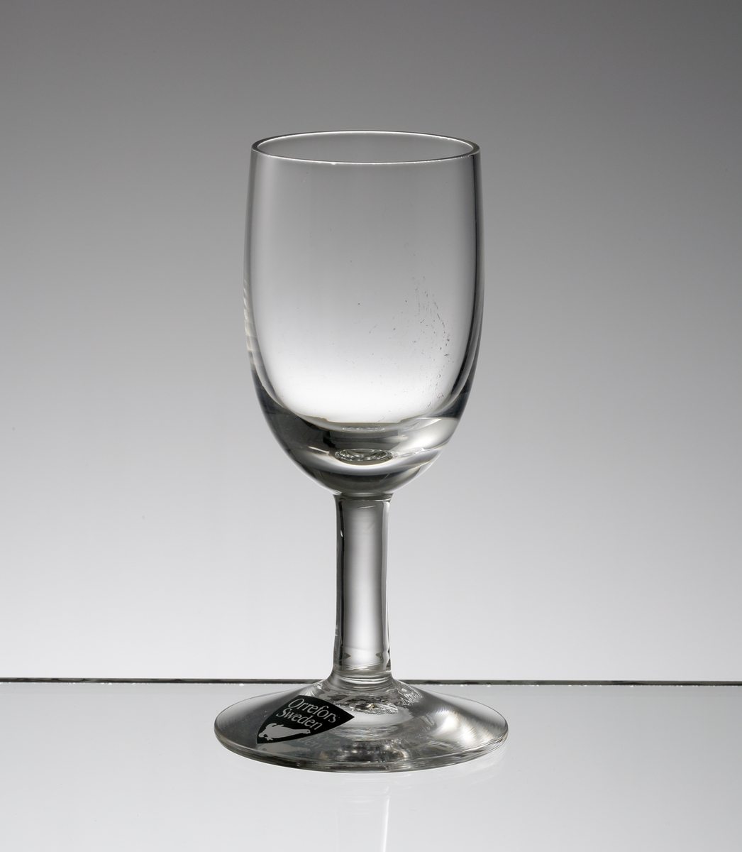 Design: Nils Landberg.
Likörglas. Ovoid slät kupa med stråben.
Fabriksmärke: mörkgrå botten med vit text.