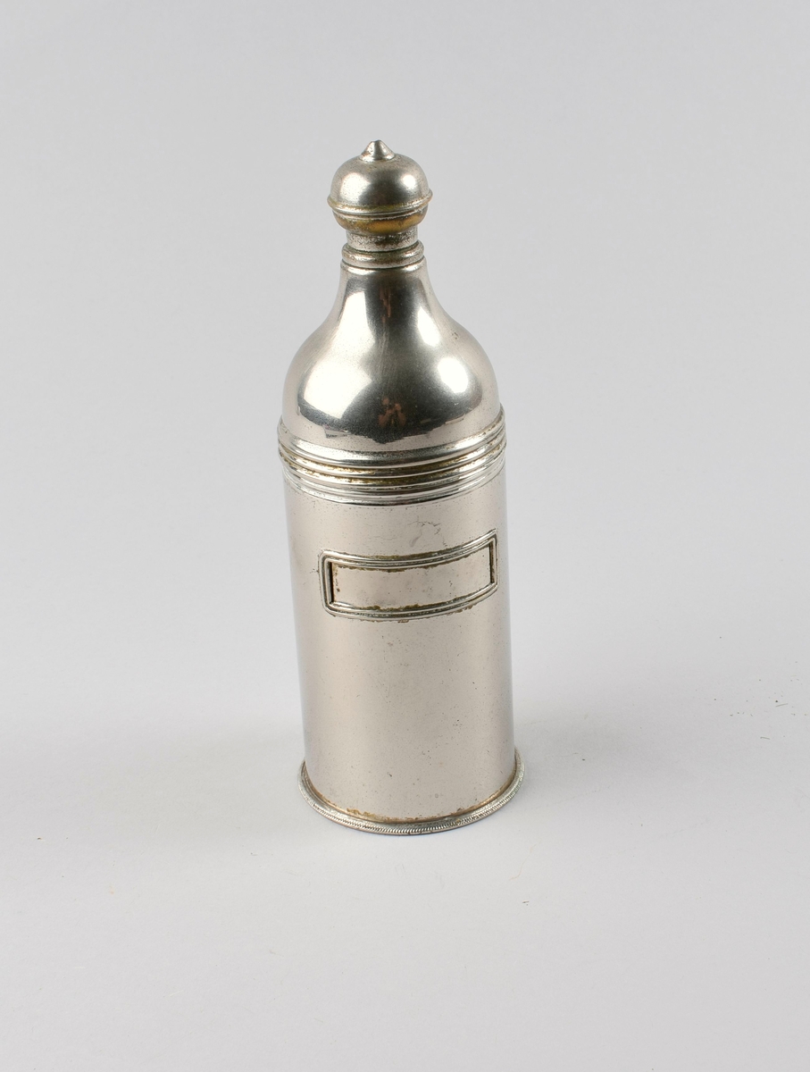 Sylinderformet flaske med kort hals og halvkuleformet dynketopp med lite hull. Innrammet rektangulært felt til etikett.
