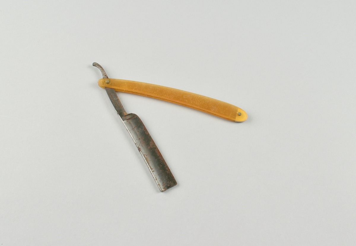 Sammenleggbar barberkniv med skaft i ravfarget materiale.