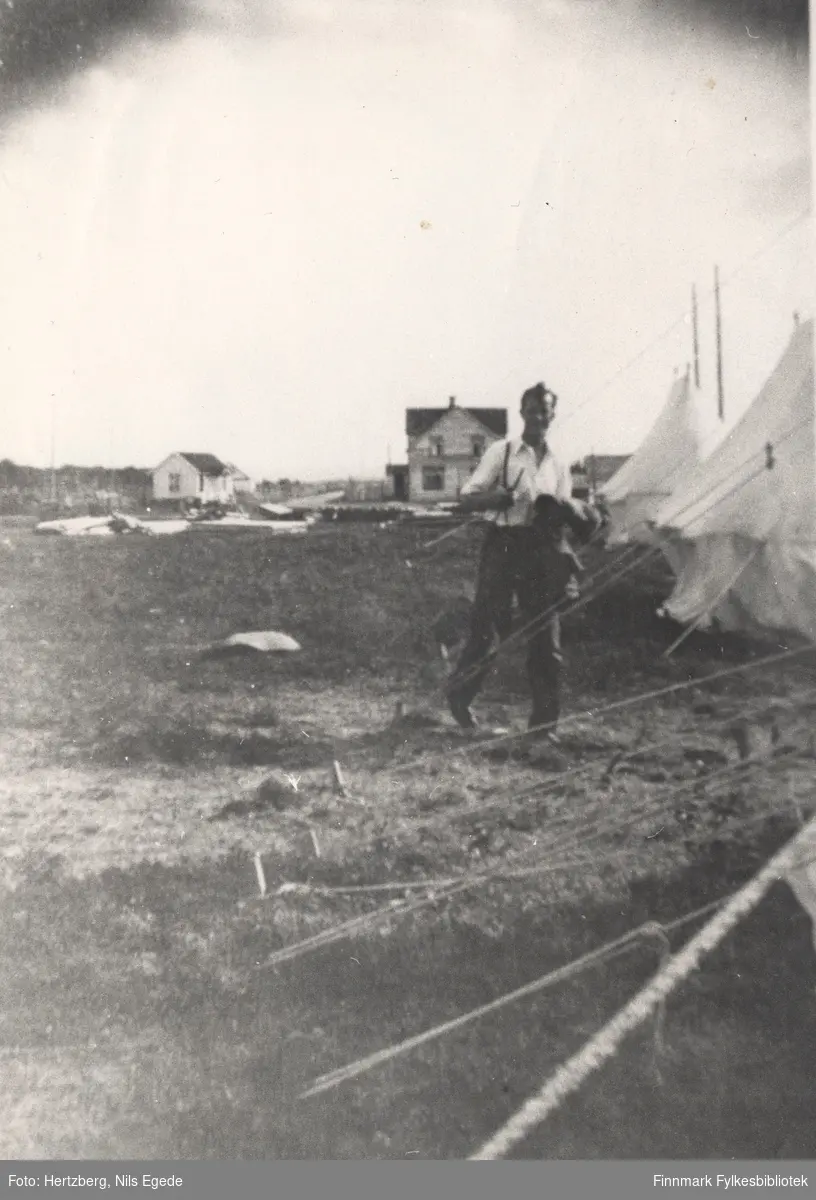 Bygging av bukkebro over Tanaelva, 1939. Pionerkompaniets leir ved Seida i Tana. Her ser vi Nils Egede Hertzberg på vei til teltet sitt. I bakgrunnen står huset til løytnant Tapio. Det ble brukt som messe for Pionerkompaniet.