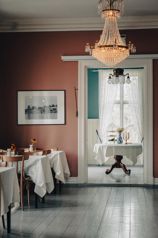 Foto av rom med stoler og bord dekket med duker. Annet rom synes gjennom dørene.