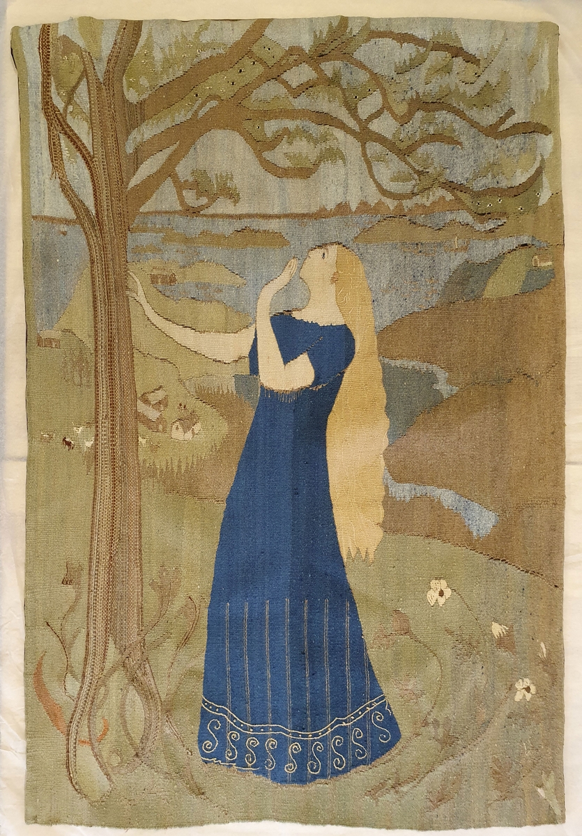 Billedvevteppe som viser en ung kvinne med langt gult hår og blå kjole, under et tre. Blomster på gresset og vann/hav i bakgrunnen. Fargene er falmet på forsiden, men sterke på baksiden.