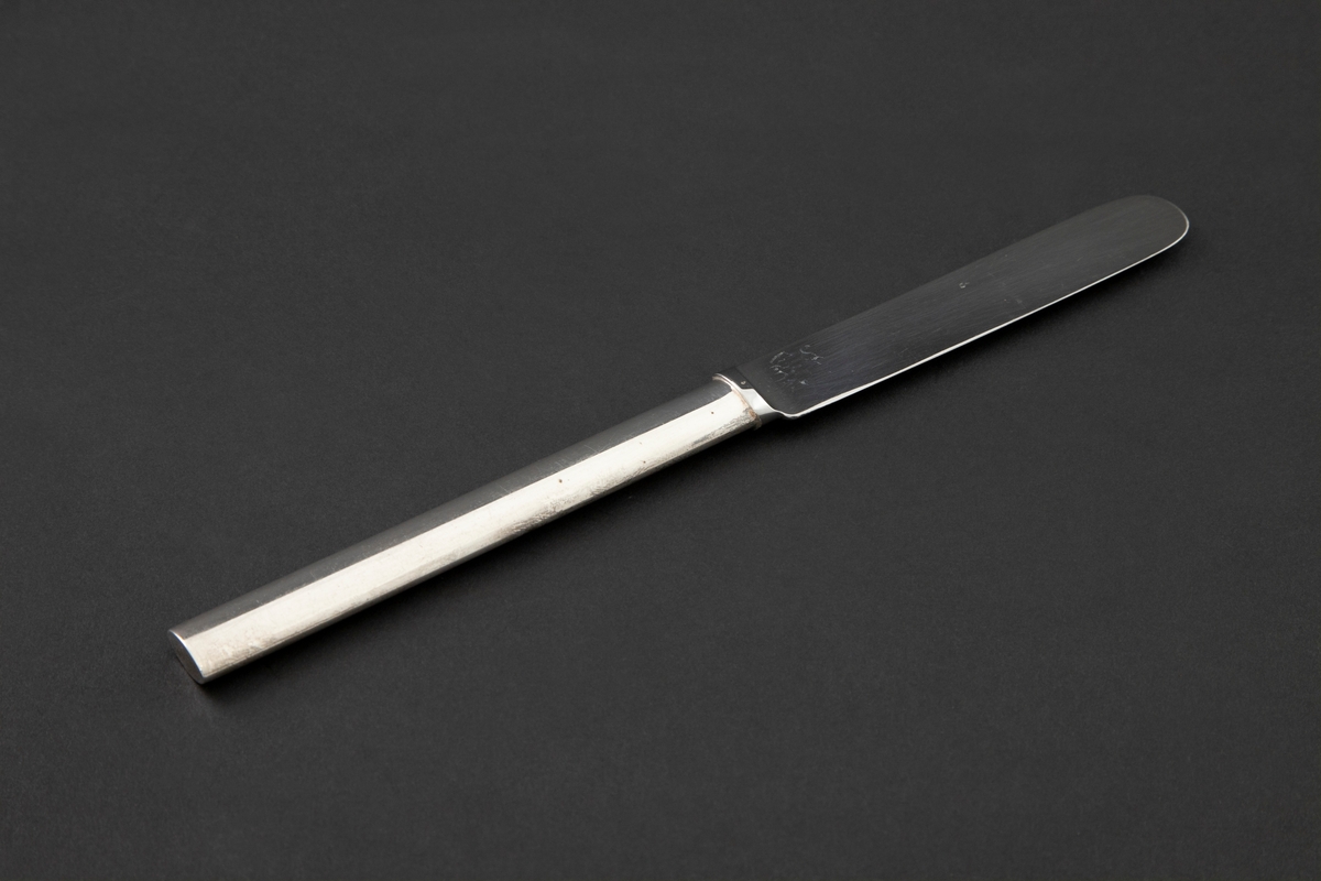 Liten kniv i sølvplett. Ovalt skaft med rett avslutning og bredere knivblad. Fra bladets halvrunde avslutning er egg og rygg parallelt.