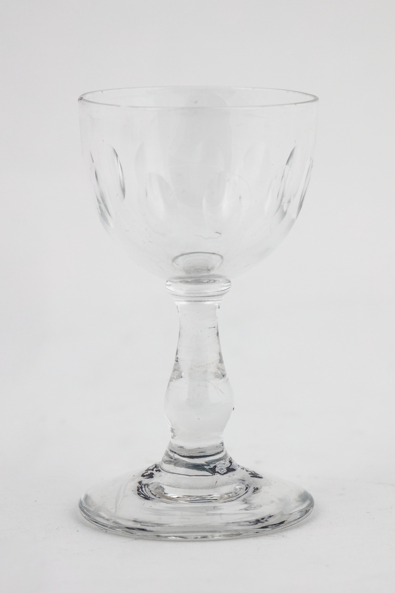 Vinglass (rødvinsglass) med rett klokke, pæreformet stett og flat fot. Enkel olivensliping rundt klokken, ellers udekorert. Klar farge. Glasset er i god stand.