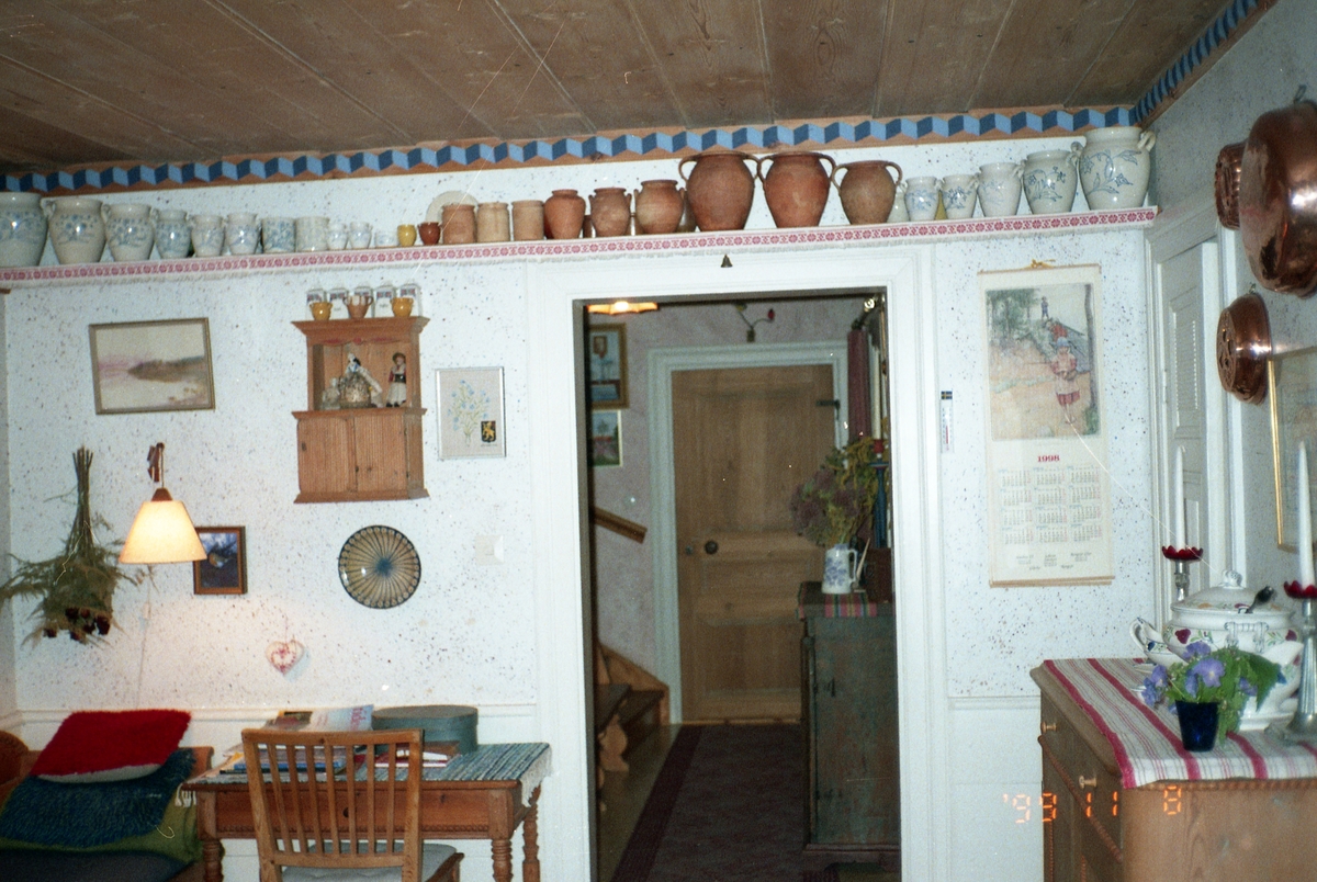 Interiör från Sunnanåker, 8 november 1999. Rum med stol, och bord. Högt upp på väggen sitter en hylla där det står många krukor uppradade.