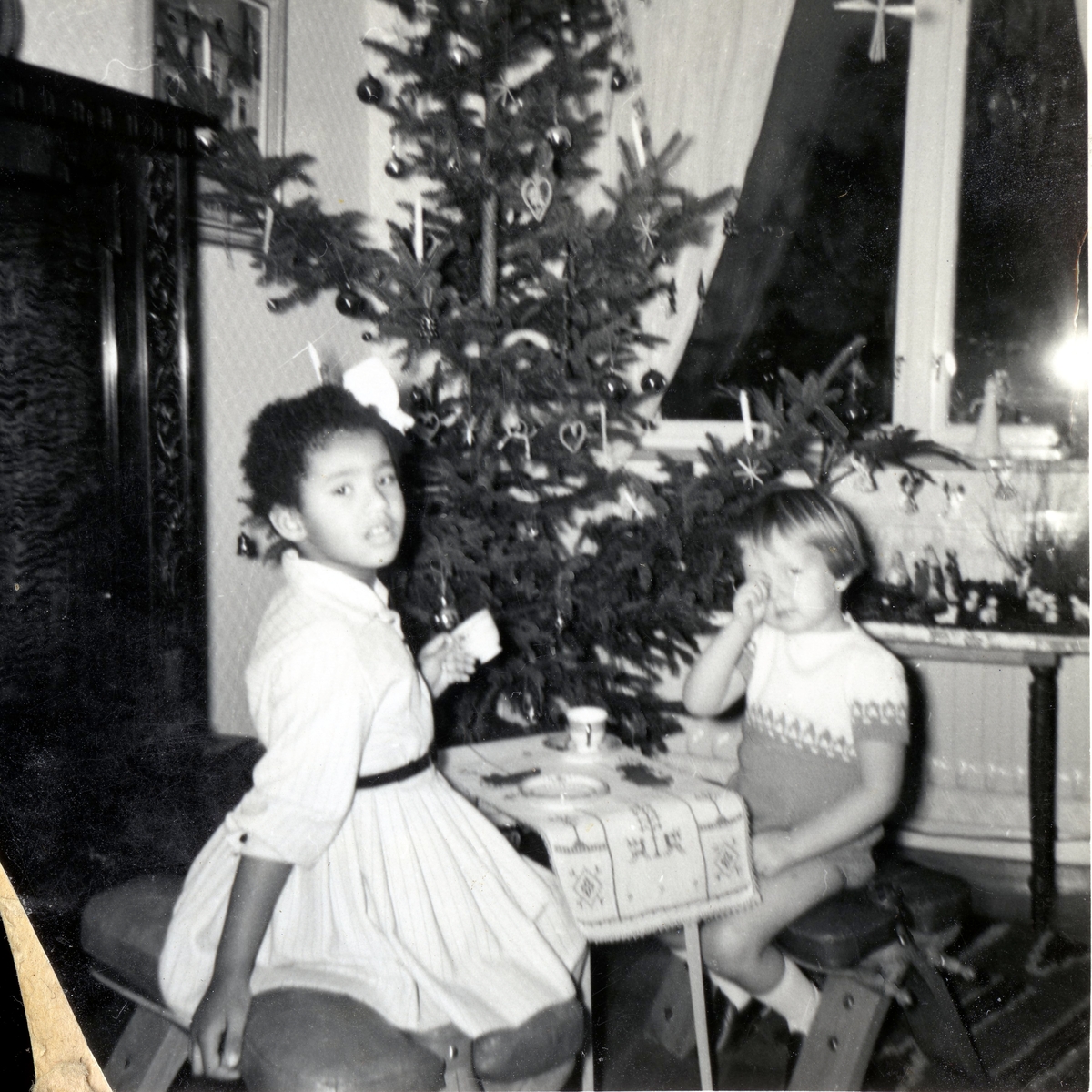 Två små vänner sitter vid ett litet bord framför julgranen och "dricker kaffe" i Manne Ekmans föräldrahem, Rothvalls hus på Streteredsvägen 31 Kållered år 1959. Från vänster: Susanne Kullbring (född 1953) och Manne Ekman (född 1955). Susanne och Manne var barndomskamrater och bodde grannar. Relaterat motiv: A2873.