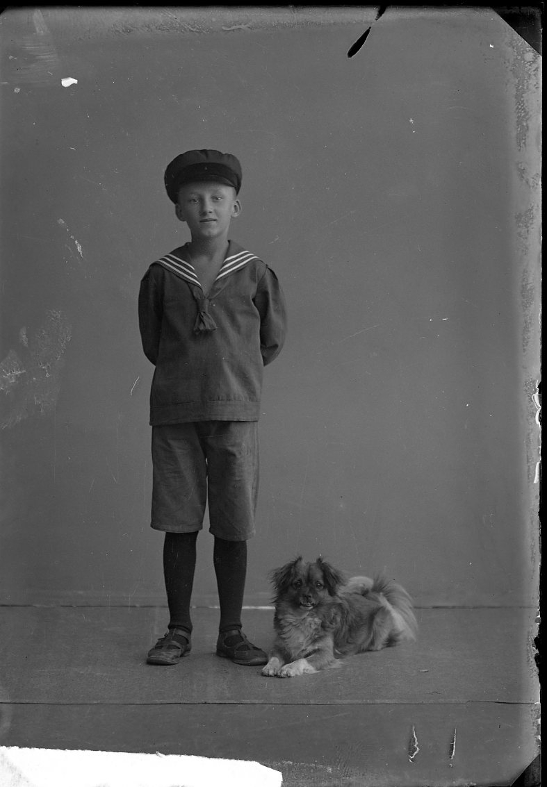 Porträtt av en pojke i keps och sjömanskostym. Pojken heter Kasper. En hund ligger vid hans fötter.