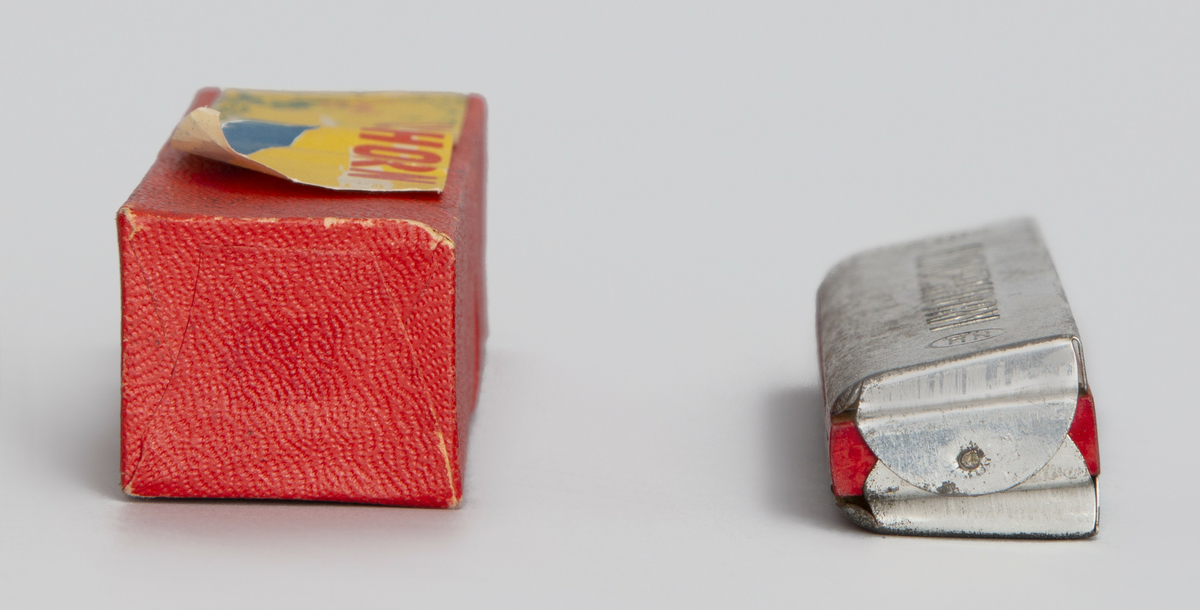 Tremolomunnspill i metall og rødmalt tre med 20 metalltunger. Medfølgende eske av kartong.
