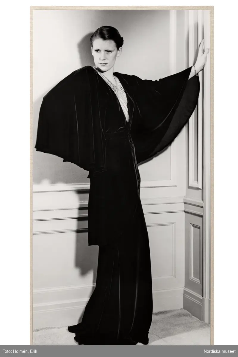 Mannekäng visar aftonklänning. Sammetsklänning med lång, mycket vid ärm, livet med infälld kil av avvikande tyg, skört och hellång kjol. NK:s Franska damskrädderi hösten 1935.