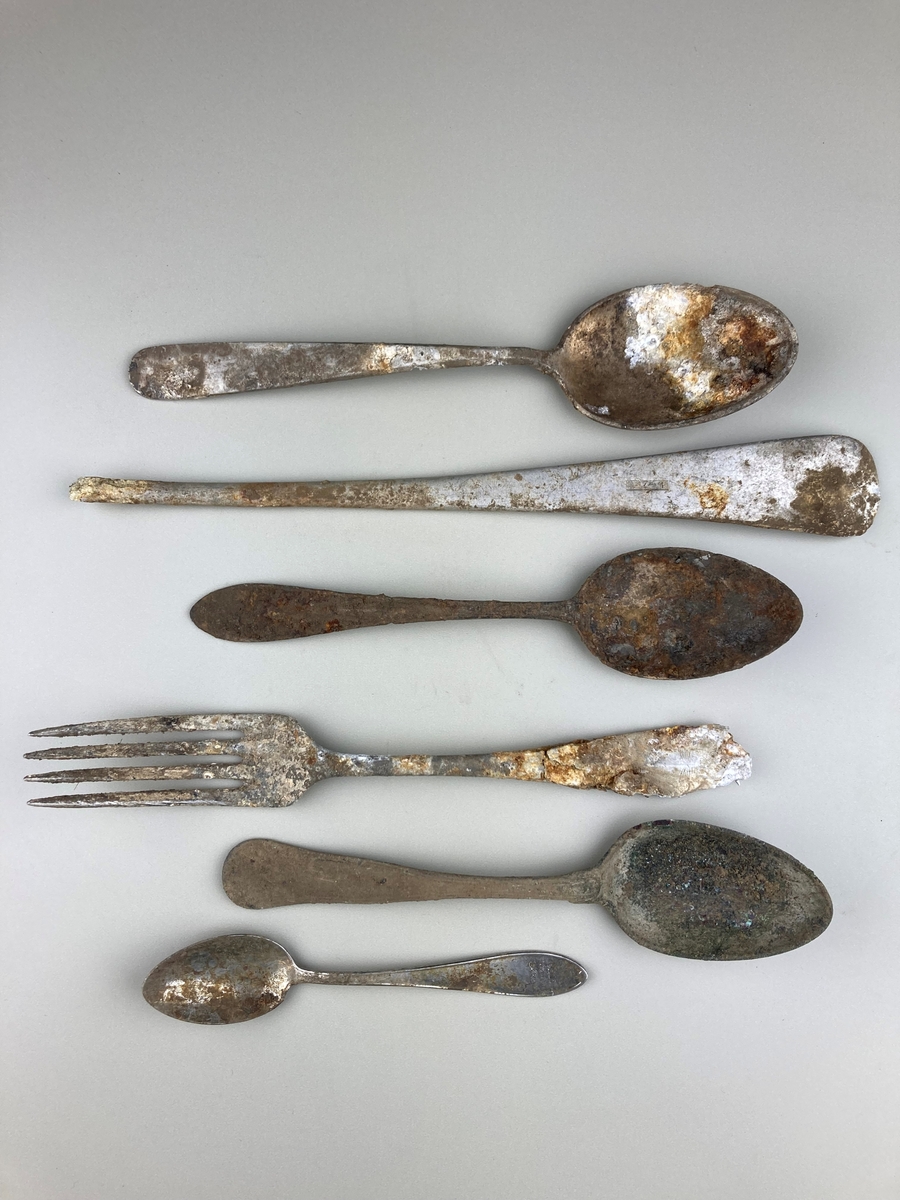 4 skjeer, 1 gaffel og 1 ukjent (kun håndtak). Alle i metall, rustet i større eller mindre grad.