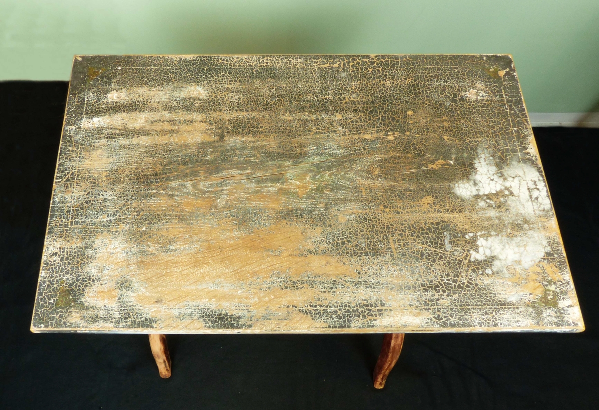 Brunmålat bord med spår av dekorationsmålning på bordsskivan. En rund slå mellan ståndarna som mynnar ut i en båge.