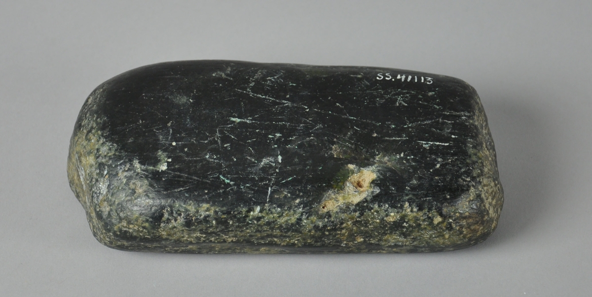 Avlang og avrundet glatt, svart stein av typen serpentinitt, med kalkstriper på langs.