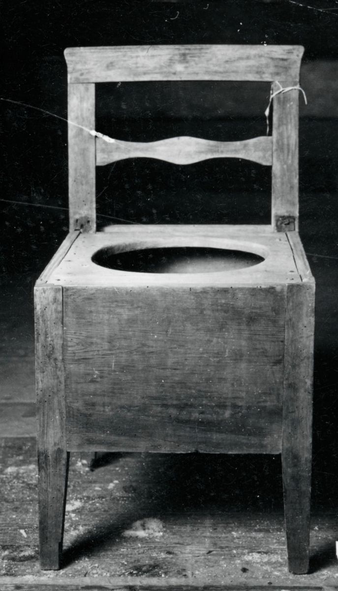 Brunmålad pottstol med kvadratisk trälåda med hål i sitsen, raka ben och rygg, genombruten rygg med horisontel tvärslå.