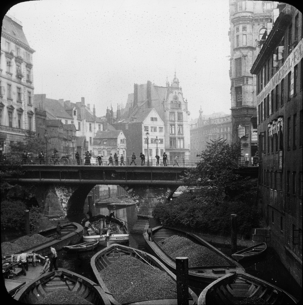 Skioptikonbild med motiv av arbete med  lastade pråmar på kanal i Hamburg.
Bilden har förvarats i kartong märkt: Resan 1906. Hamburg 9.