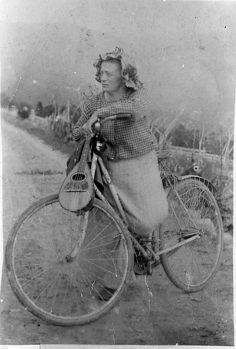 Kvinne på sykkel, med mandolin. Usikker identitet, men muligens Anna Samuelsen. Angivelig på tur over Dagalifjellet med Inga Vatnås, 1913.