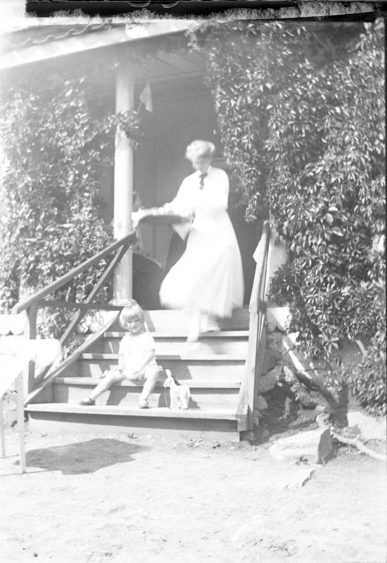 En kvinna går nerför en farstutrappa med en bricka i händerna. På nedre steget sitter ett barn med en leksakhäst. Det är sommar. Kvinnan är eller har anknytning till "friherrinnan Falkenberg" från Stockholm